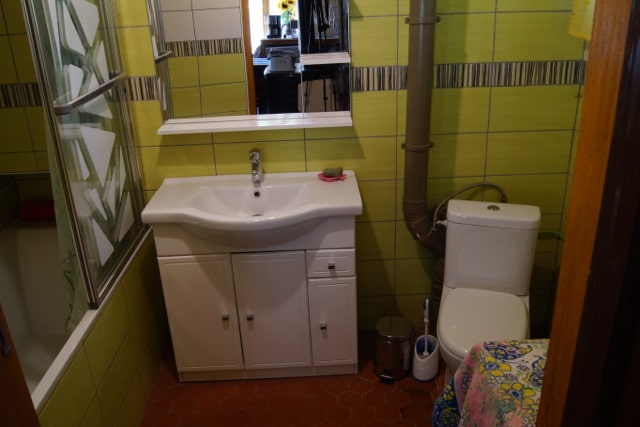La salle d'eau du rez-de-chaussée contient des toilettes, une vasque et une baignoire. Le carrelage est vert.