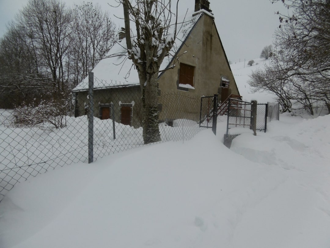 Le gîte vu de côté, en hiver. Les arbres n'ont plus de feuilles et une épaisse couche de neige recouvre le sol.